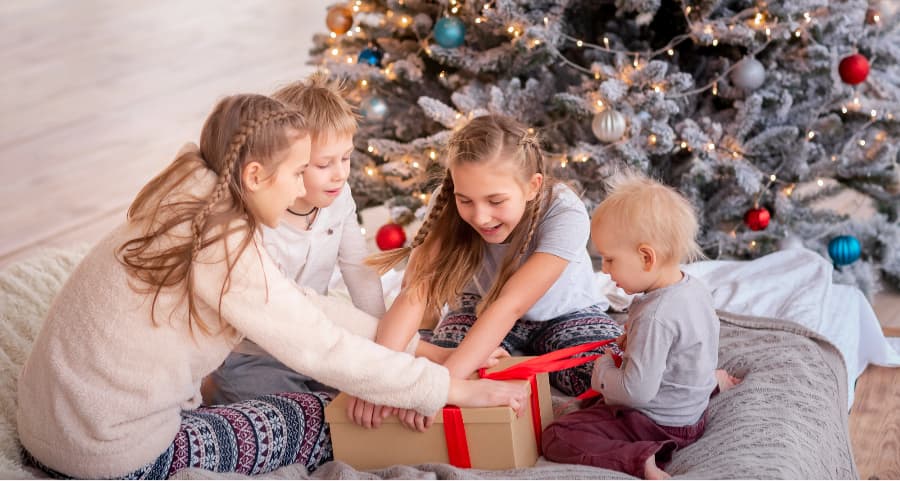 Kids opening a present near a Christmas tree.